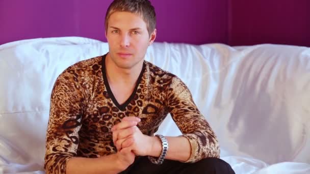 Young man in shirt poses and smiles to camera, sitting on sofa. — Αρχείο Βίντεο