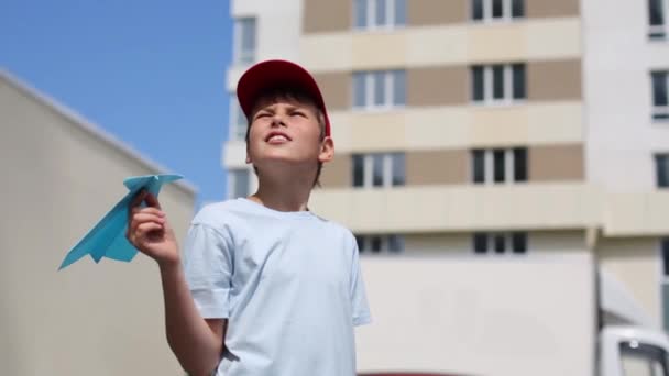 Niño en camiseta lanza avión de papel cerca de edificio residencial — Vídeos de Stock