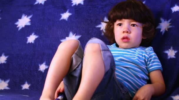 Pequeño niño se encuentra en el sofá cubierto con cobertor azul . — Vídeo de stock