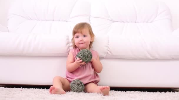 Kislány ruhában játszik, zöld szalma golyók mellett kanapé — Stock videók