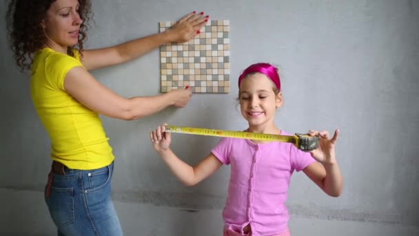 Молода жінка з дочкою вимірює плитку за правилами стрічки — стокове відео