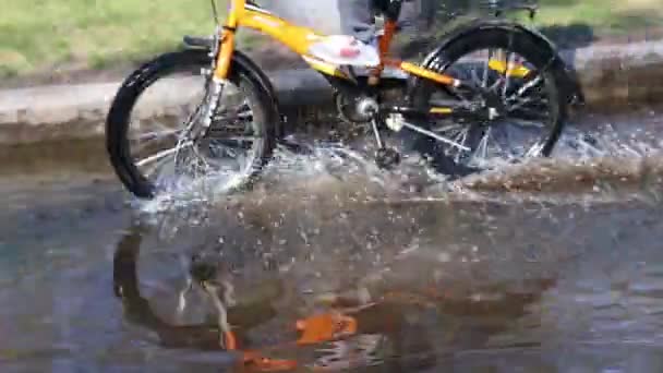 Fietser en grote plas rijden op straat op zomerdag — Stockvideo