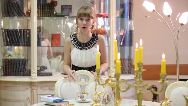 Chica declama cerca de librería de vidrio y mesa con velas — Vídeos de Stock