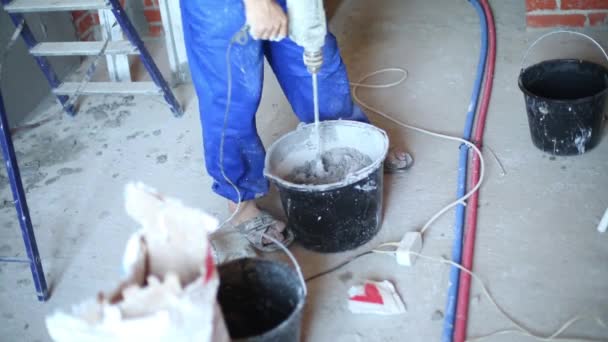 Pernas de trabalhador com misturador de mão preparando mistura para parede de gesso — Vídeo de Stock