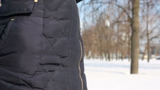 Young woman in hat shakes off the snow from gloves in park — Stockvideo