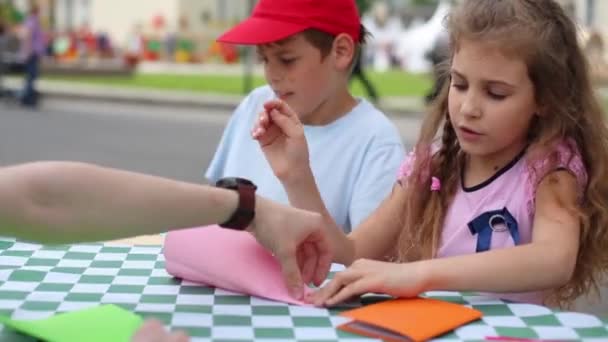 Jongen en meisje van mensen maken gekleurd papier vliegtuigen aan tafel — Stockvideo