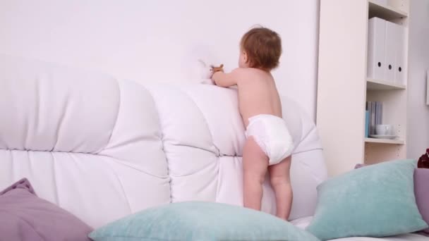 Niño en pañal juega con juguetes en sofá blanco con almohadas — Vídeo de stock