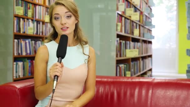 Flicka med en mikrofon i handen sitter på en röd soffa — Stockvideo