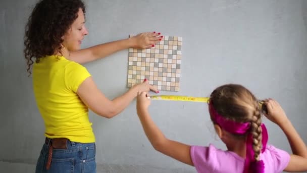 Young woman with her daughter applied to wall tiles and measuring — Stock video