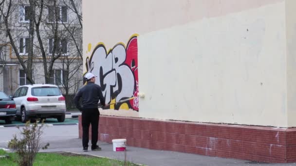 Člověk maluje přes graffiti na stěně budovy. — Stock video