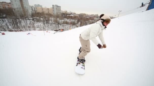 Niña snowboarder bajando por la ladera cerca de la ciudad — Vídeos de Stock