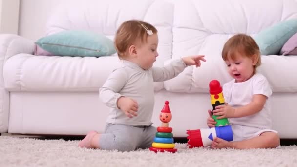 Två vackra barn sitta på mattan och spela med leksaker nära soffa — Stockvideo