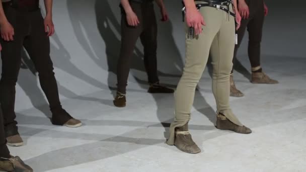 Legs of five men in hunting costumes dancing in grey studio