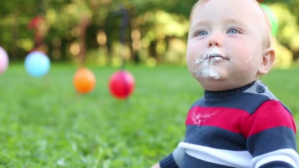Симпатичный смазанный взбитыми сливками счастливый малыш сидит в летнем парке — стоковое видео