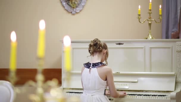 Velas ardientes y espalda de niña en vestido blanco tocando el piano — Vídeo de stock