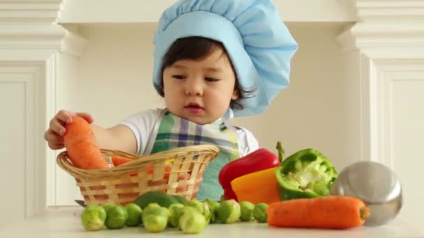 Baby pojke i kök förkläde och mössa stå nära bordet — Stockvideo