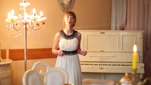 Bella ragazza in abito bianco parla vicino pianoforte bianco alla sera — Video Stock