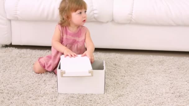 Little girl sits near white box on soft carpet and stands up — Stock Video