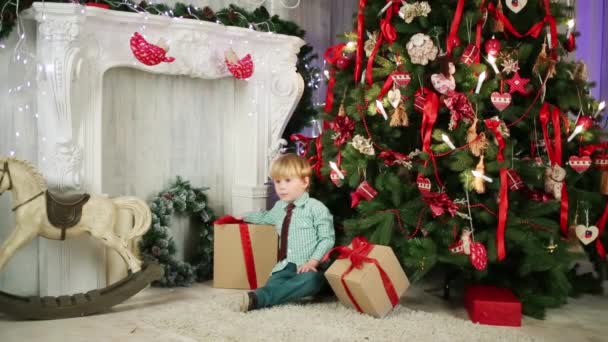 Niño pequeño se sienta con cajas de regalo — Vídeos de Stock