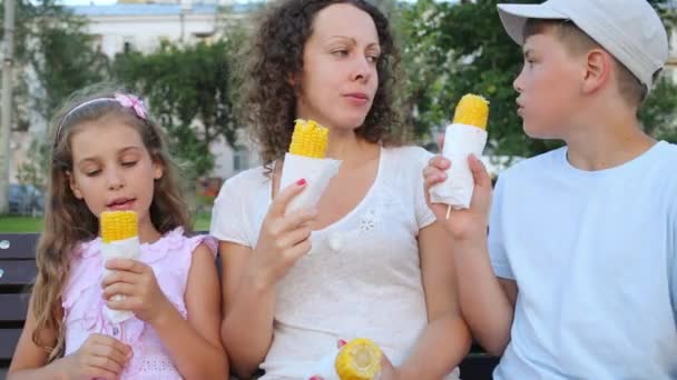 Женщина с детьми ест вареную кукурузу — стоковое видео