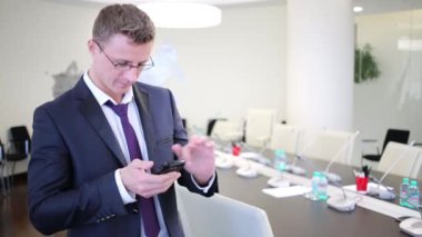 İşadamı smartphone ile toplantı odasında duruyor.