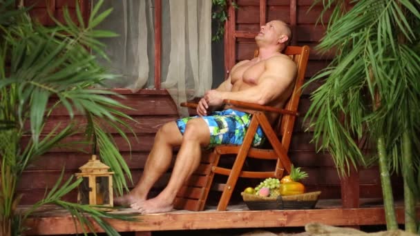 Muscular hombre se sienta en chaise lounge — Vídeos de Stock
