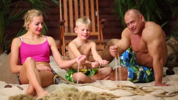 Famiglia si siede sulla spiaggia contro bungalow — Video Stock