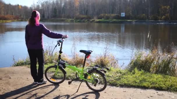 Mujer de pie con bicicleta cerca del lago — Vídeos de Stock