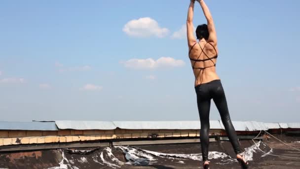 Mujer en traje negro baila en el techo en el fondo del cielo azul — Vídeos de Stock