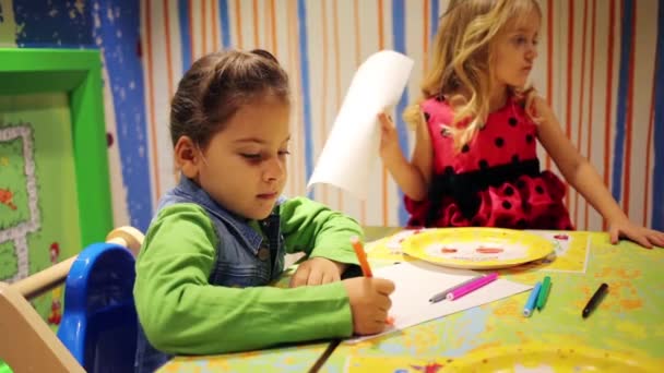Маленька дівчинка малює та інші дівчина тримає паперу — стокове відео