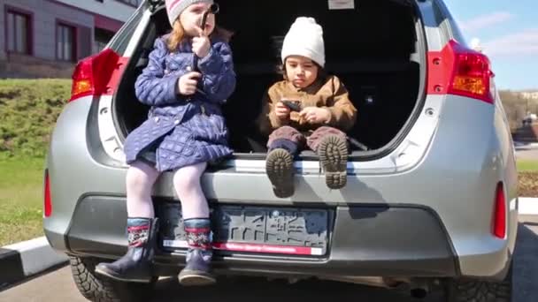 Twee kinderen in de open kofferbak van auto — Stockvideo