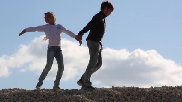 Девочка и мальчик идут по куче камней — стоковое видео