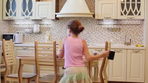 Menina serve mesa com copos na cozinha — Vídeo de Stock