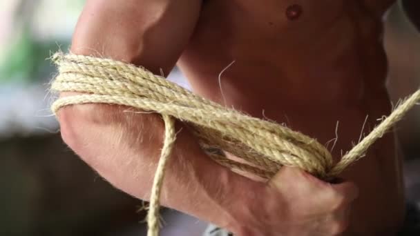 Мускулистый полуобнаженный мужчина, намотанный веревкой на руку — стоковое видео
