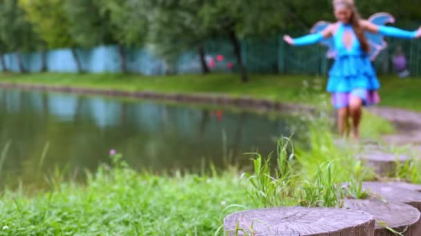 Mädchen im Feenkleid läuft auf Stümpfen am Ufer entlang — Stockvideo