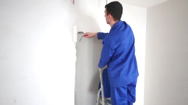 Man uitstrijkjes lijm op de muur boven de deuropening met een roller — Stockvideo