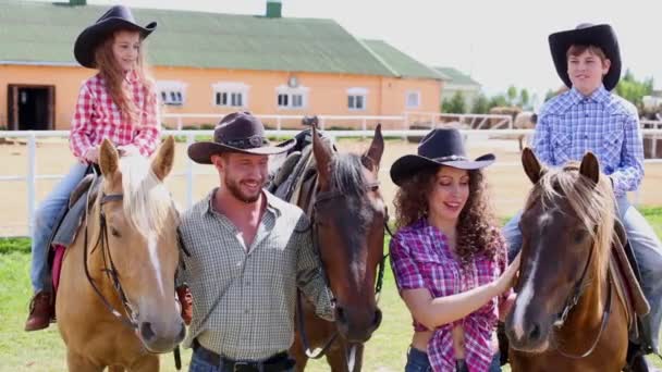 Padre y madre sostienen caballos en los que los niños se sientan — Vídeos de Stock