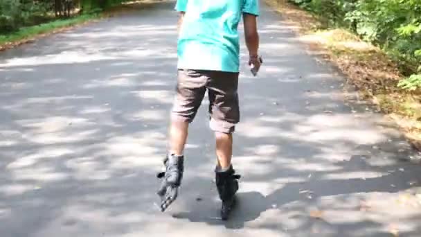 Baksidan av pojke med leksaker i shorts rullskridskoåkning i sommaren park — Stockvideo