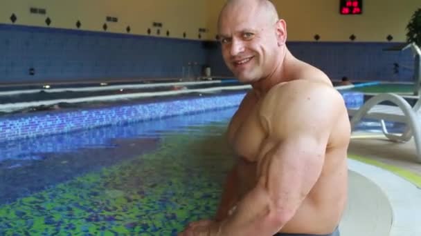 Bodybuilder sits near indoor pure pool — Stock Video