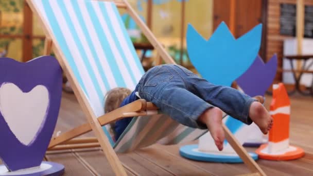 Boy tries to get out of sun lounger in cafe — Stock Video