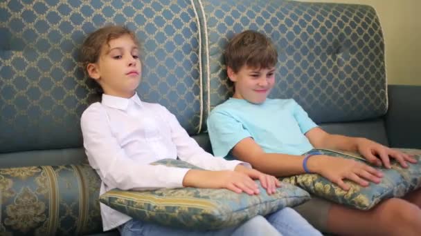 Niño y niña se sienta en el sofá — Vídeos de Stock