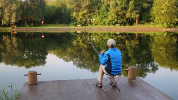 Menino senta-se perto do lago com vara de pesca — Vídeo de Stock