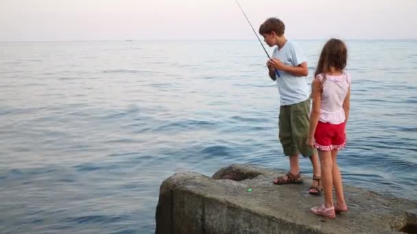 Αγόρι και κορίτσι με το ψάρεμα με καλάμι στο μπλε της θάλασσας — Αρχείο Βίντεο