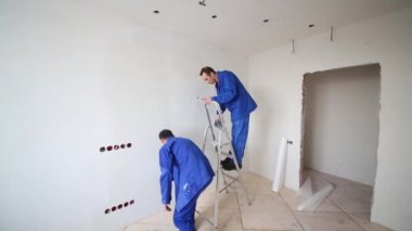 Adam aşırı fiberglas keser, sonraki adam duvara tutkal smear