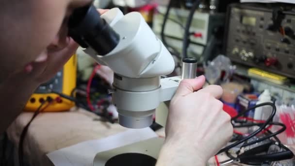 L'uomo lavora con il microscopio tra gli strumenti per la riparazione di elettronica — Video Stock