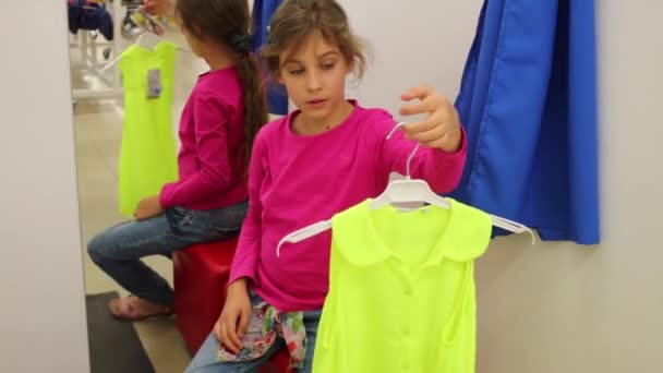 Дівчина тримає блузку в примірній кімнаті магазину — стокове відео