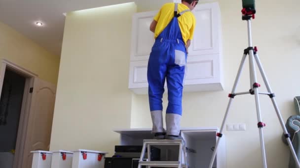 Worker on stepladder sets door to the hanging cupboard — Stock Video