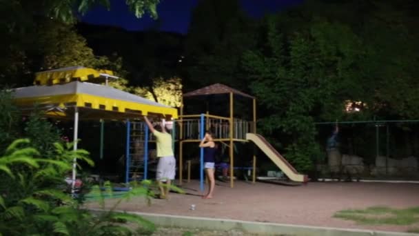 Personas con niños en el patio de recreo en la noche de verano — Vídeo de stock