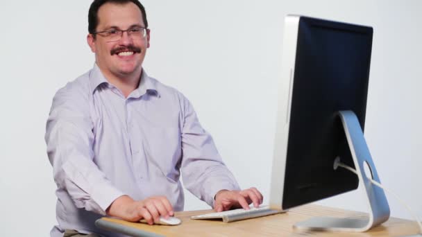 Homem satisfeito senta-se na mesa com computador, sorrisos e tipos — Vídeo de Stock