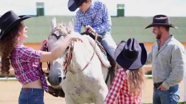 Мальчик сидит на лошади, его мать, отец и сестра стоят рядом — стоковое видео